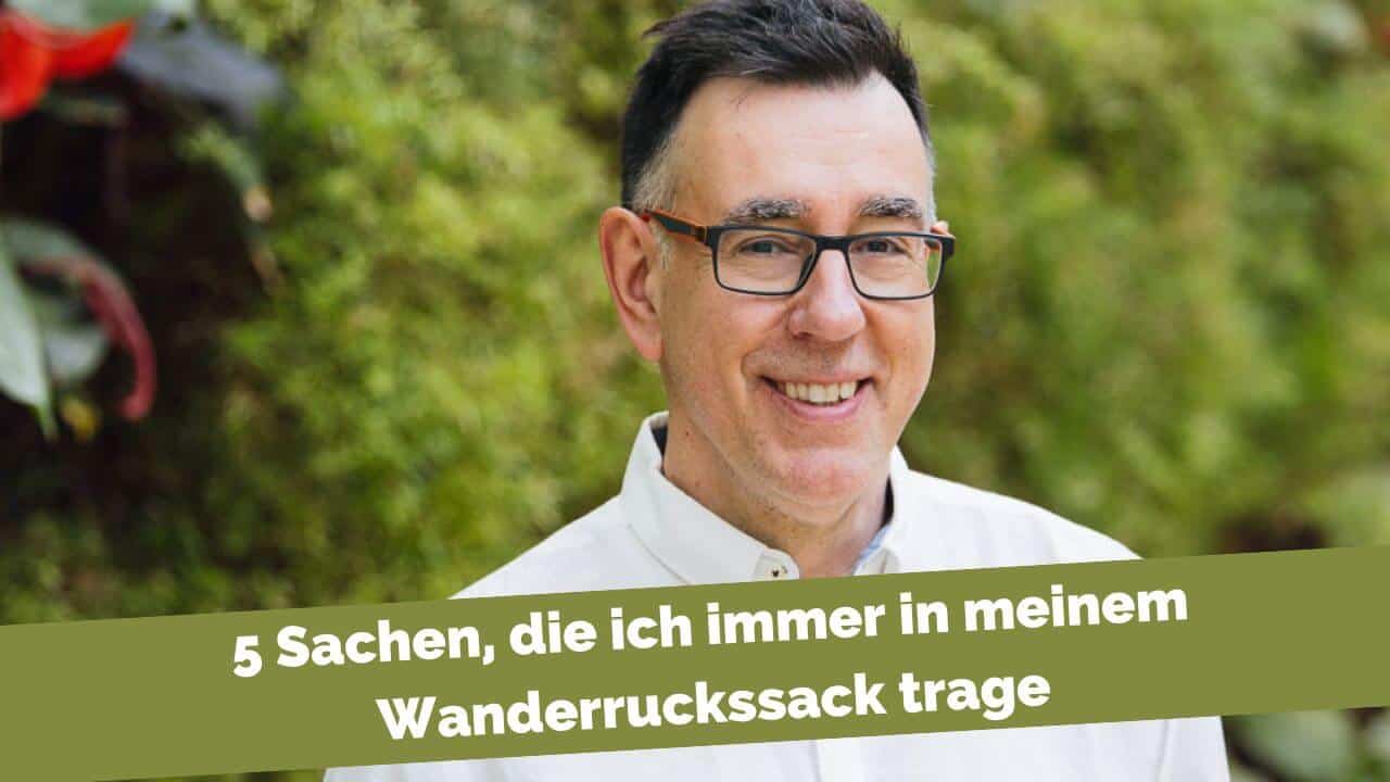 Mann vor grüner Wand. 5 Sachen im Wanderrucksack